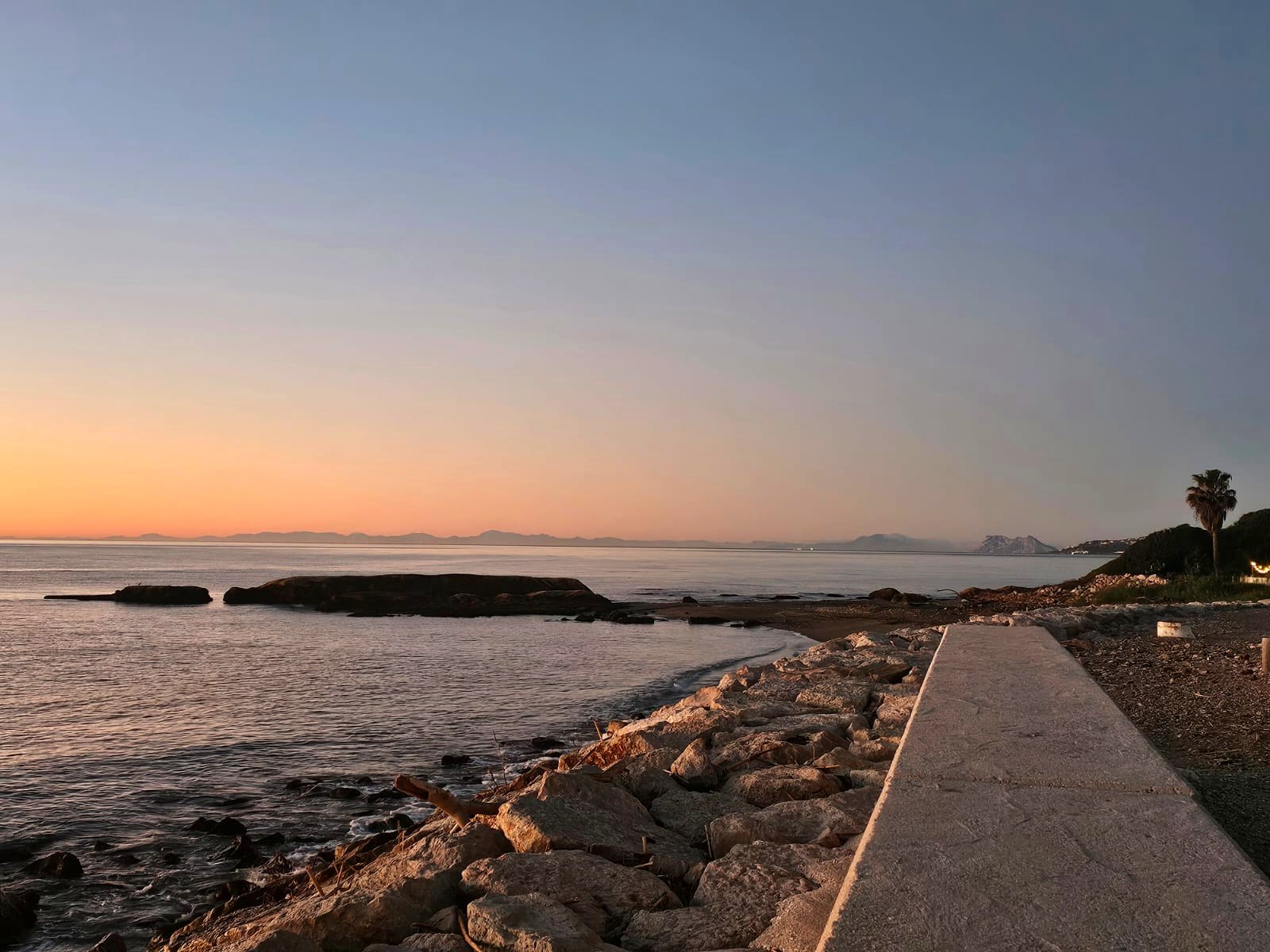 A pale dawn over a calm sea and a rocky shore