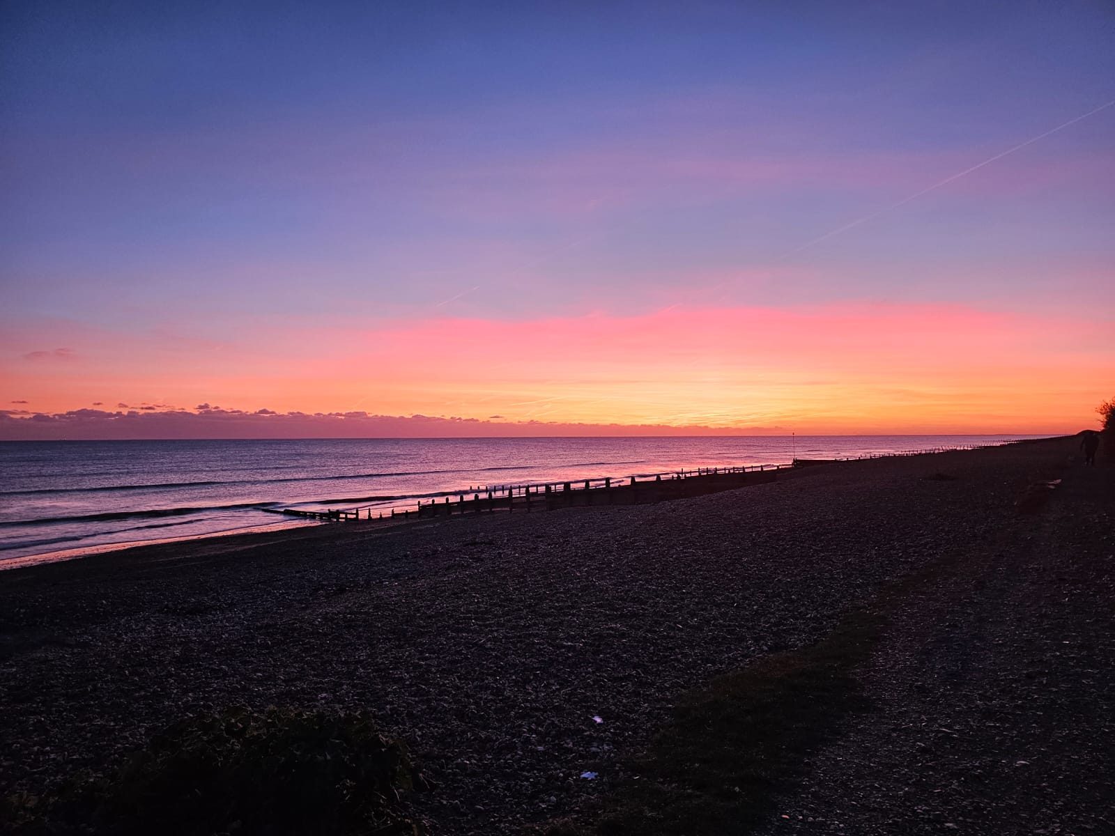 A pink and gold sunset over the sea from a shingle beach