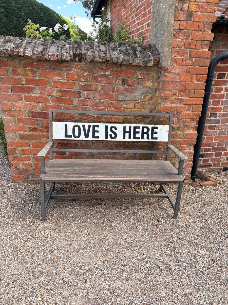 A garden bench against a brick wall with a sign reading Love is here